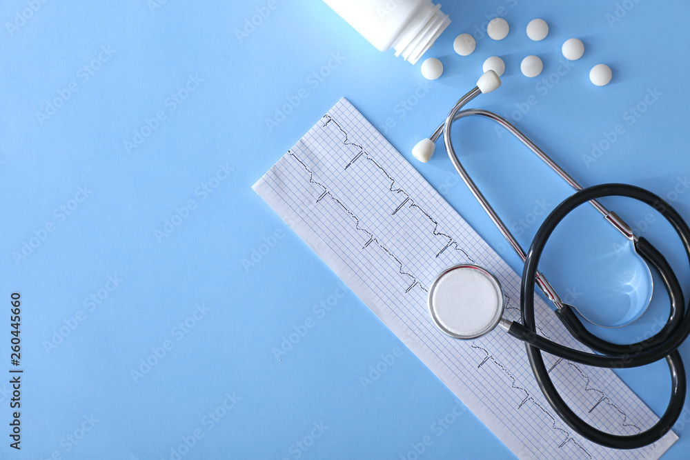 Stethoscope with cardiogram and pills on color background