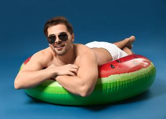 Handsome man relaxing on inflatable ring against on color background