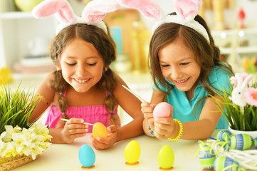 Cute two sisters wearing rabbit ears decorating Easter eggs