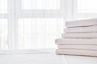 © mirage_studio - Stack of white clean bath towels on bed sheet in modern hotel bedroom interior with window on background, copy space