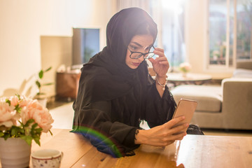 Wall Mural - Beautiful young Arab woman with eyeglasses using smart phone at home