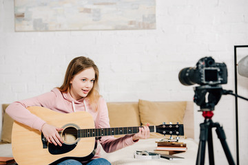 Wall Mural - Teenage blogger sitting on bed and playing acoustic guitar in front of camera