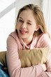 © LIGHTFIELD STUDIOS - Smiling teenage kid embracing brown cushion and looking at camera