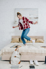 Wall Mural - Full length view of smiling teenager kid in jeans jumping on bed at home