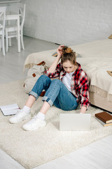 Wall Mural - Teenager with laptop and books sitting on carpet and doing homework