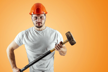 Wall Mural - Bearded Man in a helmet holds a sledgehammer on an orange background. Concept of construction, contractor, repair.