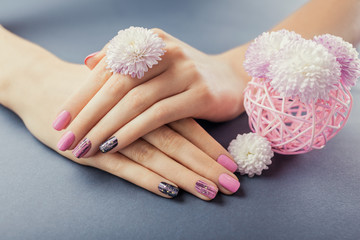 Pink and black manicure on female hands with flowers on grey background. Nail art and design