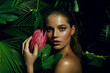 A beautiful tanned girl with natural make-up and wet hair stands in the jungle among exotic plants.