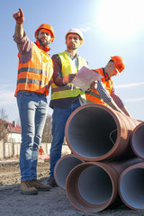 male builders workers engineers at a construction site looking drawings in helmets