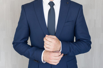 torso of anonymous businessman wearing beautiful fashionable classic navy blue suit against grey bac