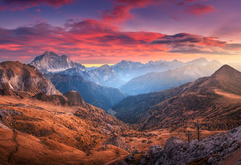 Wall Mural - Colorful red sky with clouds over the beautiful mountains in fog at sunset in autumn. Dolomites, Italy. Landscape with mountain range, hills with orange grass, trees, sky with orange sunlight. Travel 