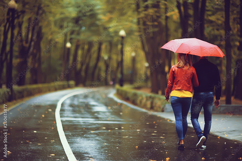 rain in the autumn park / young 25 years old couple man and woman walk ...