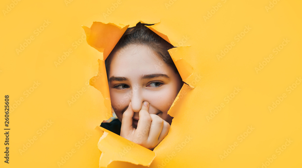 Ridiculous teenage girl closes her nose with her fingers because she feels a fetid odor. Yellow background, copy space. The concept of bloating, indigestion, farting. - obrazy, fototapety, plakaty 
