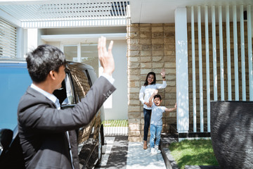 asian husband waving goodbye to his wife and child before going to work