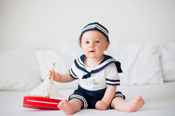 Wall Mural - Cute baby boy, dressed in marine clothes, playing with wooden boat