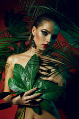 Wall Mural - A beautiful tanned girl with natural make-up and wet hair stands in the jungle among exotic plants.