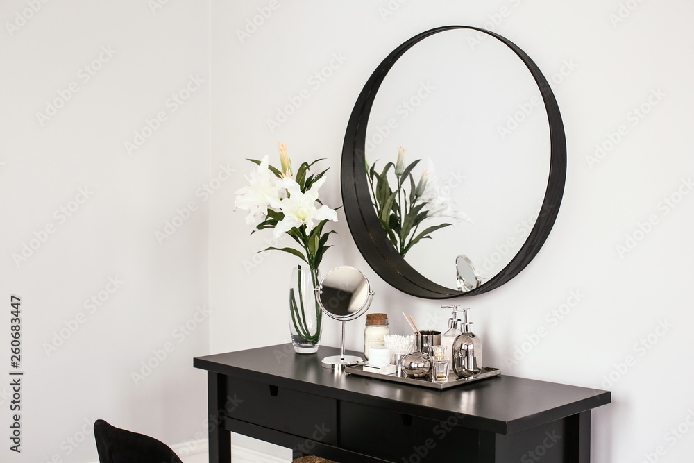Table with cosmetic products and mirror in light room