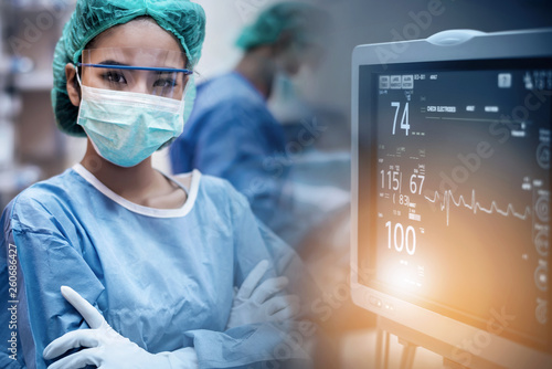 Cuadros en Lienzo Team of doctors or surgeons with electrocardiogram monitor in hospital surgery operating emergency room showing patient heart rate, during coronavirus or covid-19 crisis, medical concept