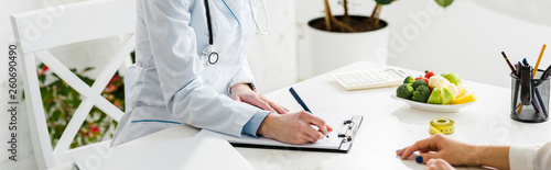 Fotomural panoramic shot of nutritionist writing diagnosis near patient