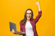 © denis_vermenko - Portrait of an excited young beautiful girl holding laptop computer and celebrating success isolated over yellow background.
