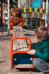 A little boy is playing on a playground with a teddy bear.