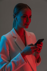 Wall Mural - Image closeup of caucasian woman 20s wearing earpods holding and using mobile phone while standing under neon lights