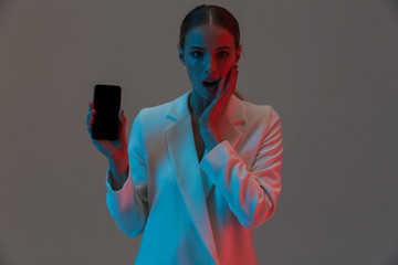 Wall Mural - Image closeup of trendy woman 20s holding mobile phone and showing black screen while standing under neon lights