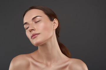 Pretty young woman with closed eyes standing against gray background