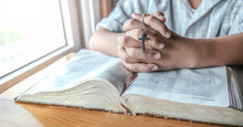 Close Up Hands Of Boy Holding Silver Cross And Praying On Holy Bible. Religion Concept.