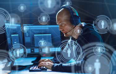 cybercrime, hacking and technology concept - male hacker in headset with progress loading bar on computer screen wiretapping or using virus program for cyber attack in dark room