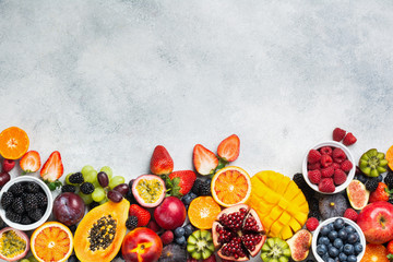 Healthy raw rainbow fruits background, mango papaya strawberries oranges passion fruits berries on oval serving plate on light kitchen top, top view, copy space, selective focus