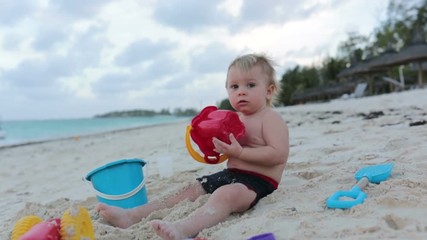 Wall Mural - Cute toddler baby boy playing with beach toys on tropical beach