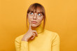 Woman portrait. Emotion. Pensive girl in eyeglasses is looking upward and thinking, on a yellow background
