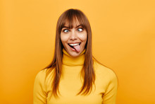 Woman Portrait. Fun. Cheerful Young Woman Is Grimacing And Showing Her Tongue At Camera, On A Yellow Background