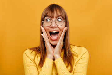 Woman portrait. Emotion. Surprise. Beautiful young woman in eyeglasses is feeling surprised, on a yellow background