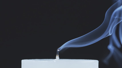 Close up shot of a white candle that has been blown out and is smoking on a black background.