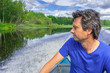 © Tatyana_Andreyeva - Handsome middle-aged man sitting at boat stern, floating along northern river and relaxing on beautiful landscape background in summer day. Travel concept. Chernaya river, Karelia, Russia