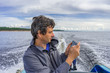 © Tatyana_Andreyeva - Handsome middle-aged man sitting at boat stern, floating along northern lake and using smartphone on beautiful landscape background in summer day. Travel concept. Onega lake, Karelia, Russia