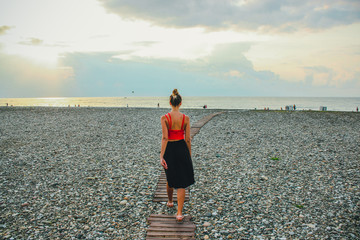 Wall Mural - Young attractive girl in a red shirt walking on the road near the sea in the summertime, Batumi, Georgia