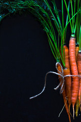 Fresh carrots and carrot stalks on black  background; flat lay; organic veggetables