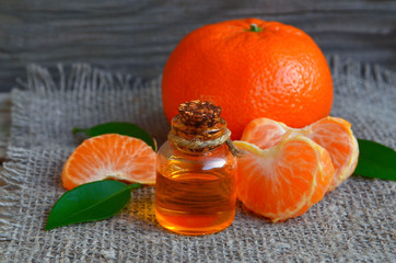 Tangerine essential oil in a glass bottle with fresh fruits on old wooden table. Ripe orange mandarin with leaves and citrus organic oil for spa,skin care,  massage and aromatherapy.Selective focus. 