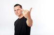 © Kiryl Lis - Young attractive man wearing black shirt showing fuck you sign over white wall background.