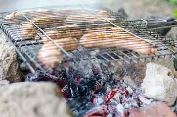 picnic with roasted sausages on red hot coals with smoky on a green natural background