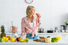 Attractive Blonde Woman Drinking Tasty Smoothie Near Ingredients In Kitchen