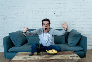 Wall Mural - Excited young man sitting on the couch watching football. Sports supporters and fans concept