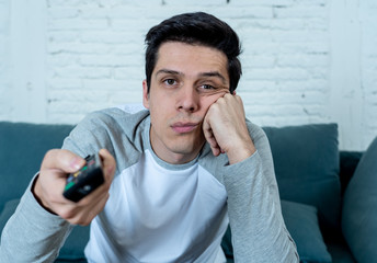 Wall Mural - Close up of bored young man sitting on the couch watching TV. Technology overuse concept