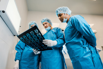 Wall Mural - low angle view of handsome and beautiful doctors in uniforms and medical masks talking about x-ray