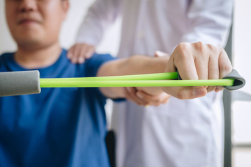 Wall Mural - Doctor physiotherapist assisting a male patient while giving exercising treatment on stretching his arm with exercise band in the clinic, Rehabilitation physiotherapy concept