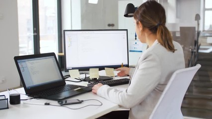 business, programming and technology concept - female programmer with notebook, sticky notes and computer working at office