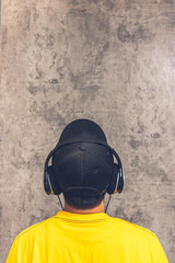 back of asian teenager with headphone listening music on grunge texture cement wall background